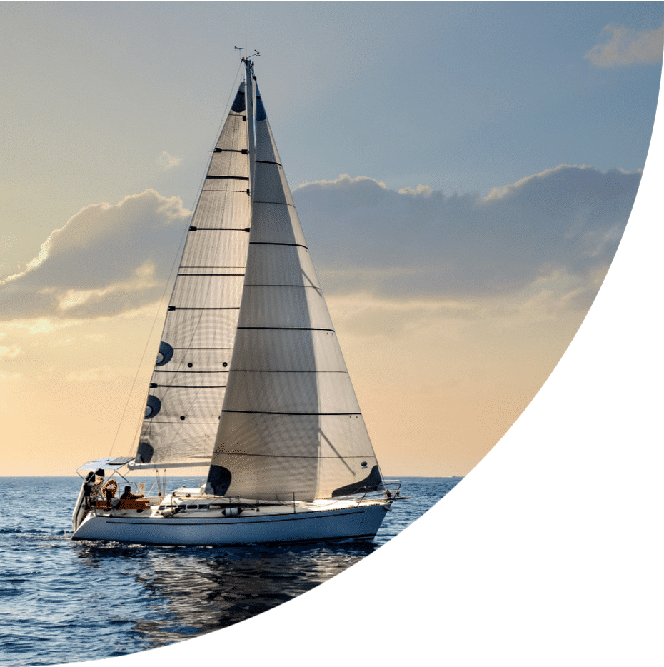 Barca a vela navigando in mare con il cielo arancione e le acque calme che riflettono la luce del sole