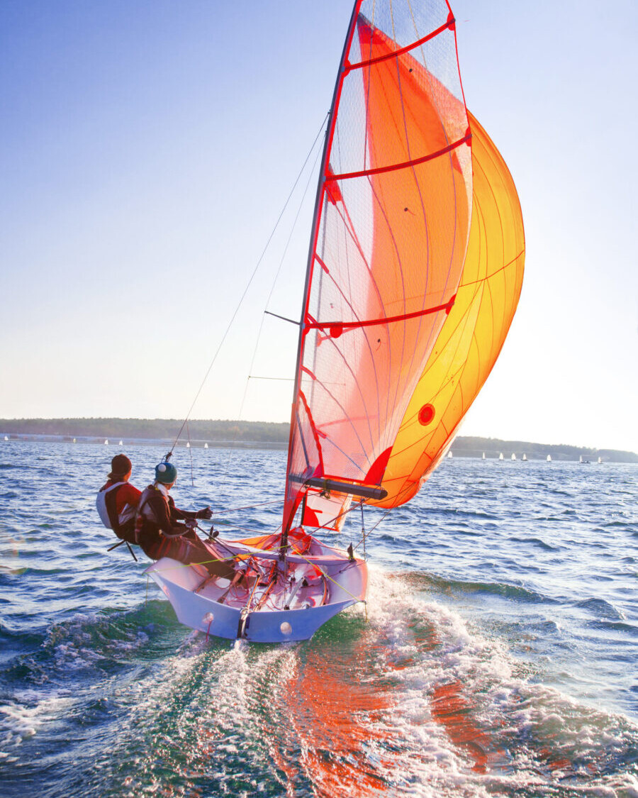Barca a vela in competizione durante una regata, con vele gonfiate dal vento e scia visibile mentre naviga velocemente sul mare.