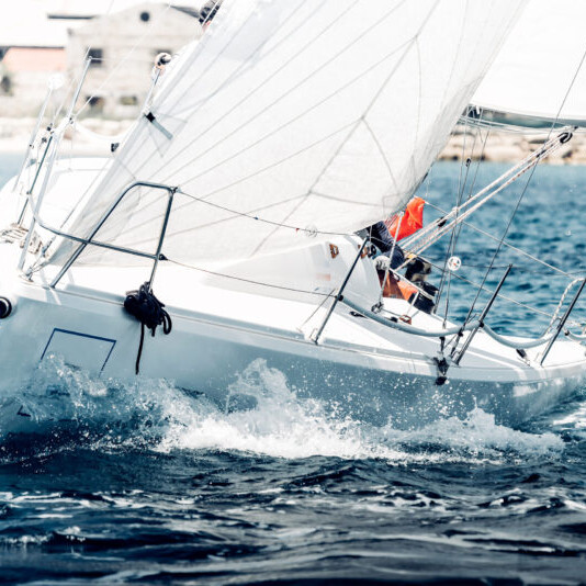 Barca a vela in competizione durante una regata, con vele gonfiate dal vento e scia visibile mentre naviga velocemente sul mare.